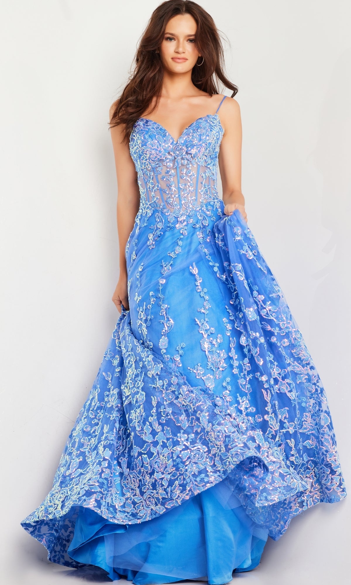 A woman in the Long Prom Dress 29072 by Jovani, a strapless turquoise blue ball gown with a sheer bodice and floral sequin embroidery, stands against a plain background holding part of her skirt.
